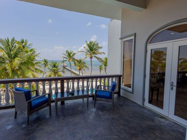 Balcony seating with ocean view and palm trees under clear sky.
