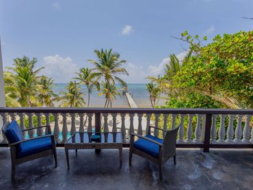 Balcony seating with ocean and palm tree view under a clear sky.