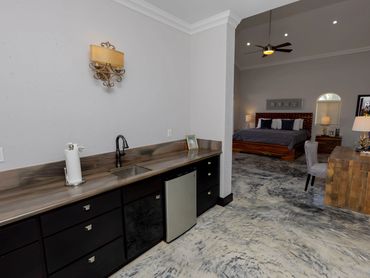 Modern room with kitchenette and bedroom area featuring a ceiling fan and wooden furniture.