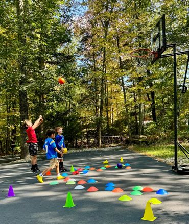 Three boys playing basketball outdoors with colorful cones on the ground.
