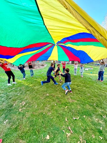 Children playing with a colorful parachute outdoors on a grassy field.