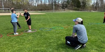 Children and an adult engage in outdoor activities with colorful hoops on grass.