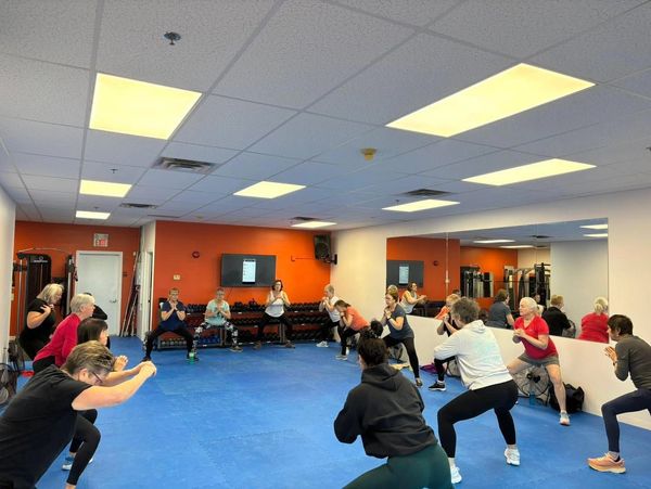 Group fitness class doing squats in a gym with blue floor.