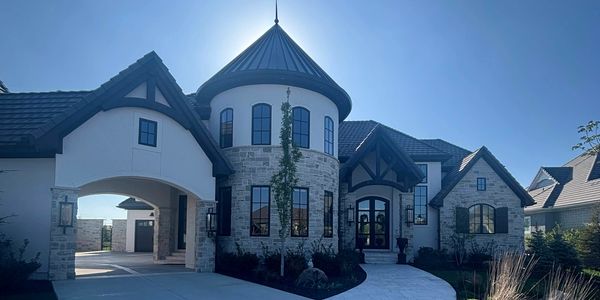 Large modern house with turret and arched entrance under clear blue sky.