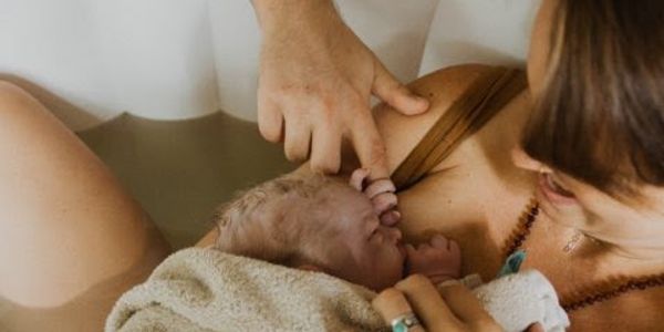 Newborn 10 lb baby born in the water in birth pool caught by father sibling holding hand