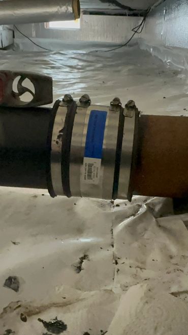 Pipe connection sealed with metal clamps in a basement.