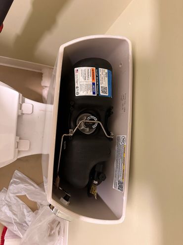 Open toilet tank showing internal flush mechanism and labels.