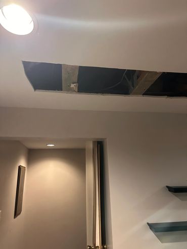 Ceiling with a rectangular hole exposing wooden beams.