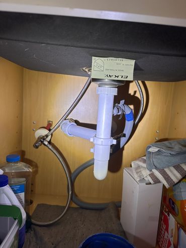 View under a kitchen sink showing plumbing and storage items.