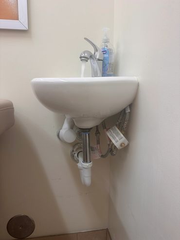 Small bathroom sink with running water and soap dispenser.