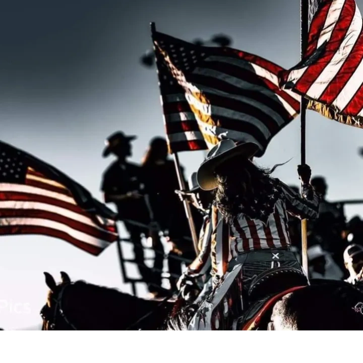 Cowgirl waving American flags at an outdoor event with silhouettes in the background.
