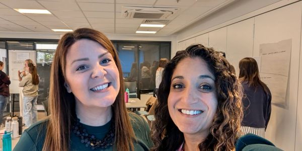 Two women smiling for a selfie in an office.