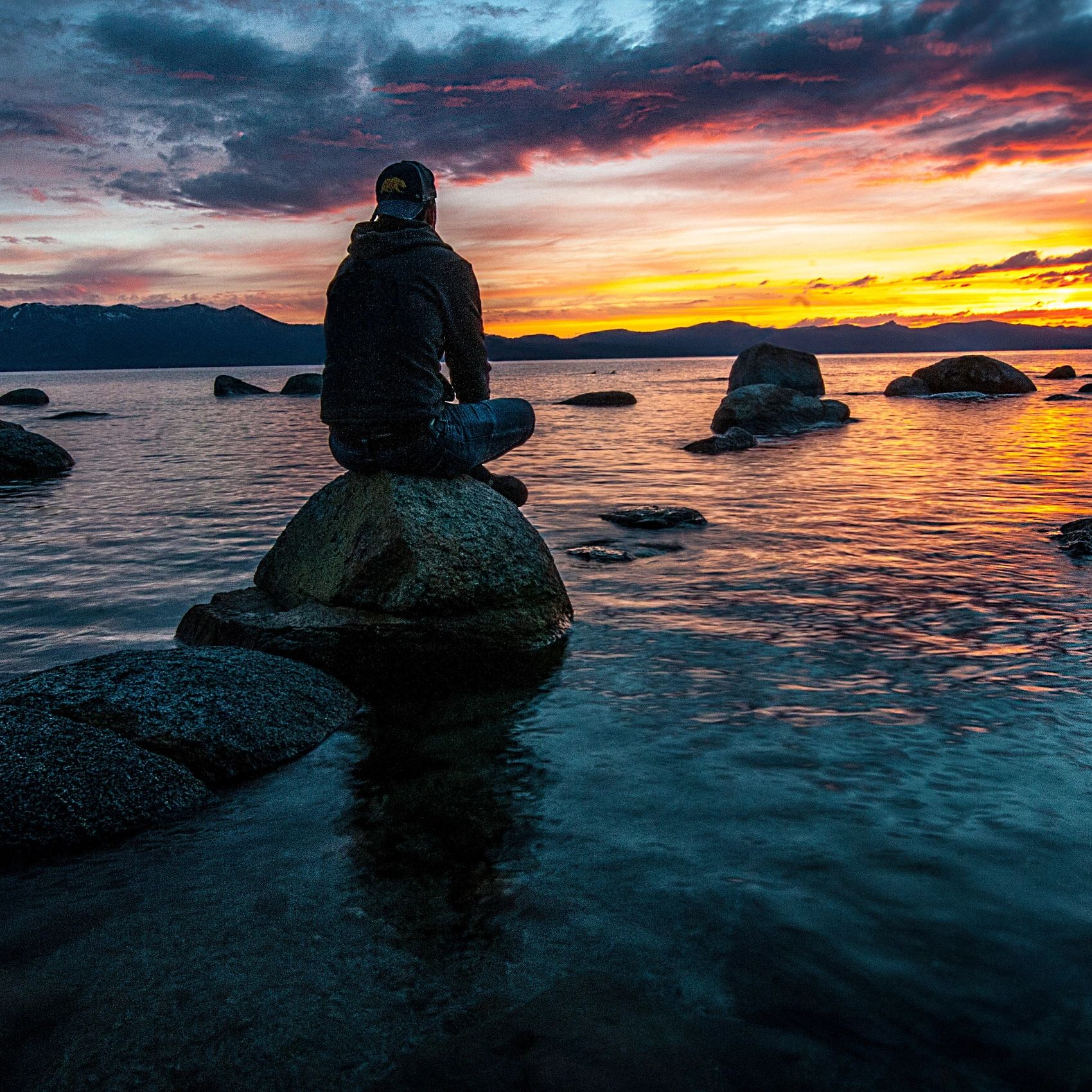 Man sitting on a rock near the water as the sun sets