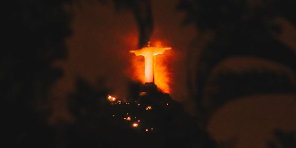 Christ the Redeemer statue glowing at night with silhouetted trees.
