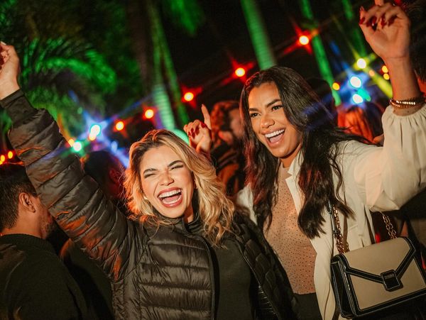 Two joyful women dancing and celebrating outdoors at night under colorful lights.