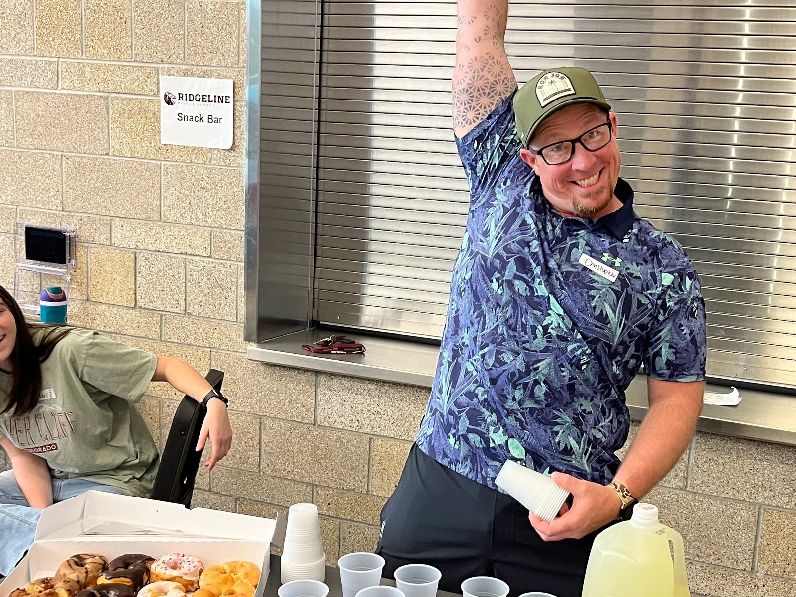 Man smiling and raising an arm at a snack bar with donuts and lemonade.