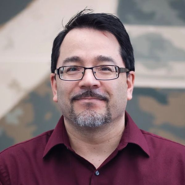 Man wearing glasses and maroon shirt smiling.