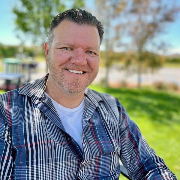 Smiling man outdoors in a plaid shirt.