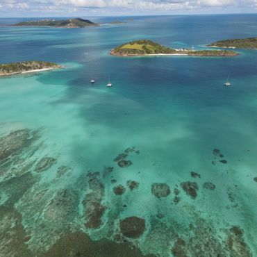 Aerial view of turquoise waters and small islands with sailboats.