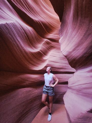 Person stands in a narrow, glowing slot canyon with smooth, flowing rock walls.