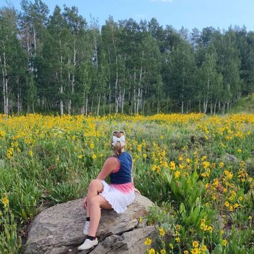 Woman sitting on a rock in a field of yellow flowers with a forest backdrop.