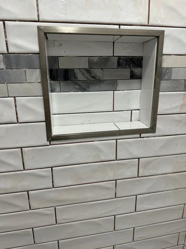 A tiled bathroom niche with mixed gray and white rectangular tiles.