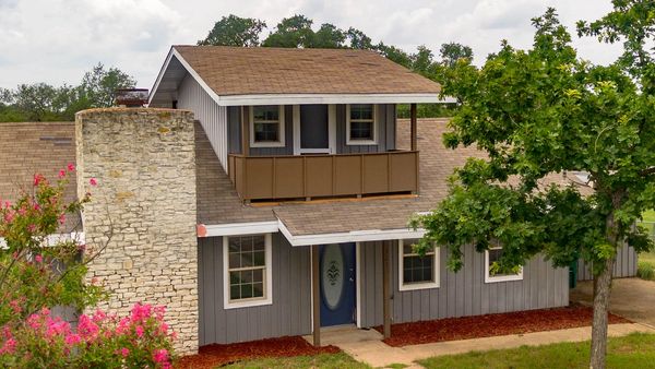 Two-story house with stone chimney and surrounding greenery.