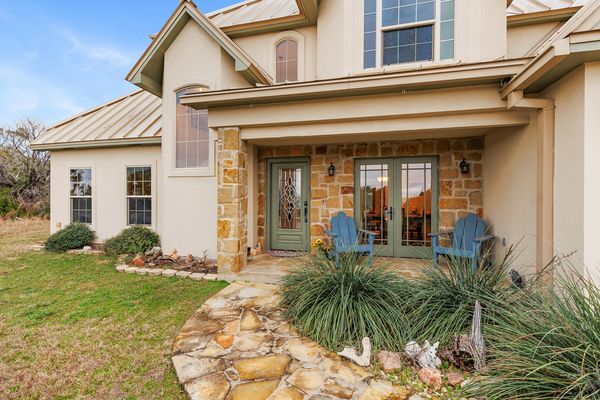 Stone porch with blue chairs and green doors at a suburban home.