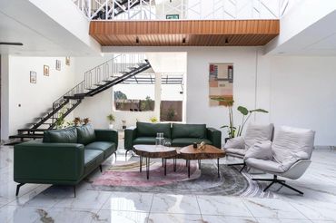 Modern living room with green sofas, unique wooden coffee tables, and white cushioned chairs on a patterned rug.