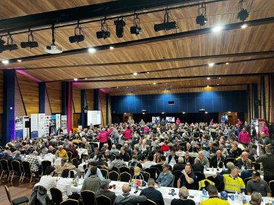 Crowded indoor event with people seated at tables in a large hall.