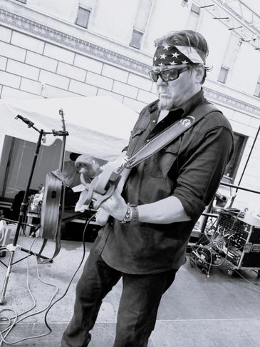 Musician playing electric guitar on an outdoor stage.