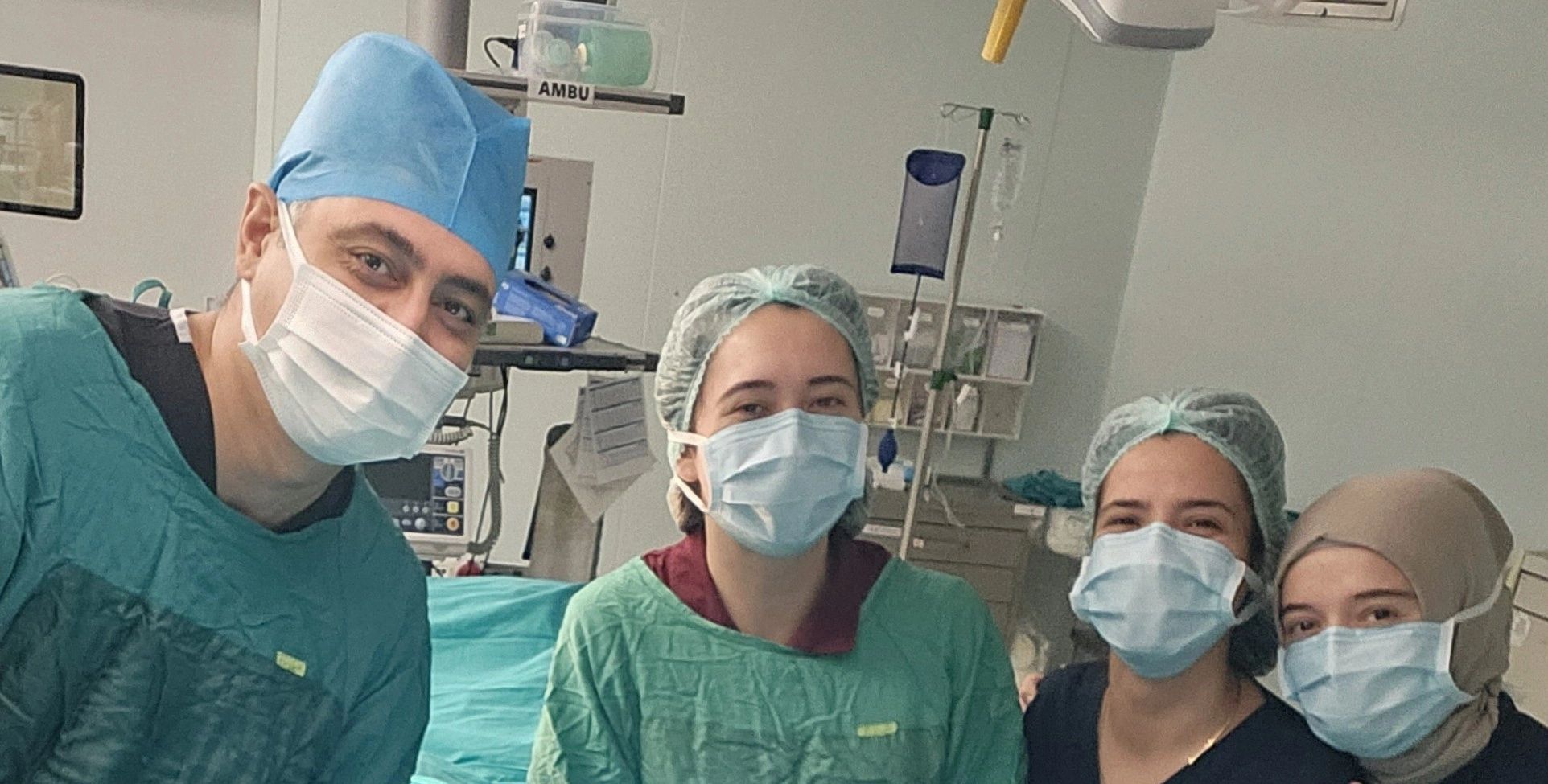 Four healthcare workers in surgical attire and masks posing together in a medical setting.