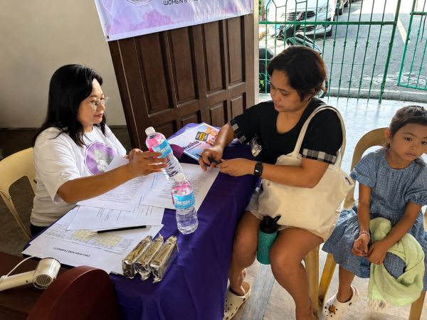 Woman receiving a water bottle and signing papers at a registration table.