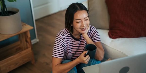 Woman smiling with coffee mug looking at laptop.