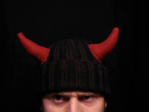 obscured face with intent eyes wearing a knit hat with devil horns.