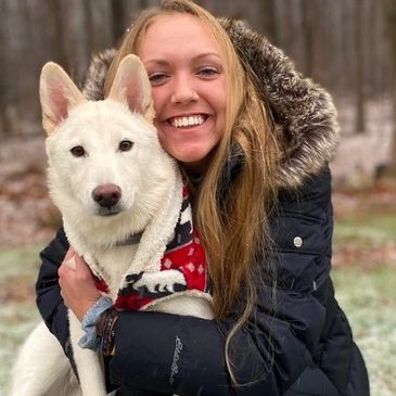 Woman hugging a white dog outdoors.