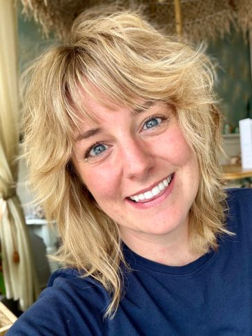 Smiling woman with blonde hair and blue eyes in a casual setting.