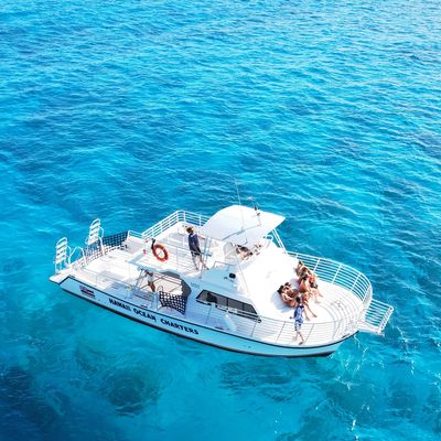 White charter boat sailing on clear blue ocean water.