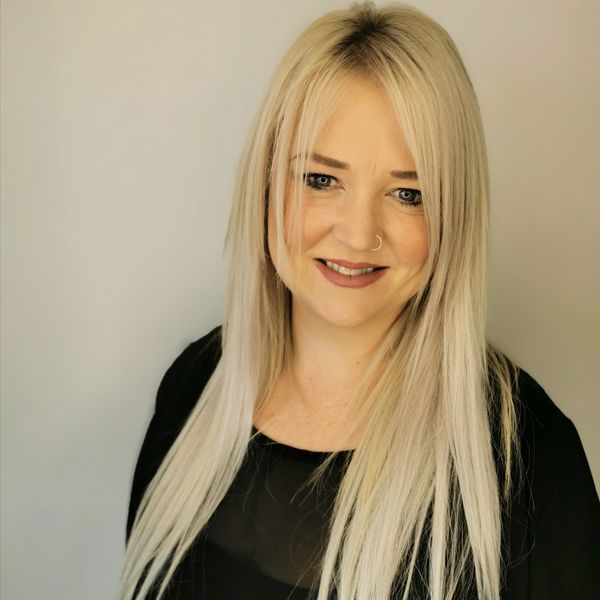 Smiling woman with long blonde hair and a nose ring in a black top.