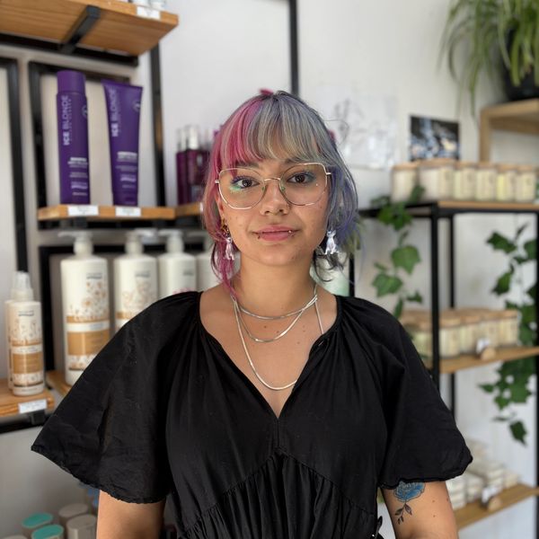 Young woman with pink and blue hair wearing glasses and a black dress.