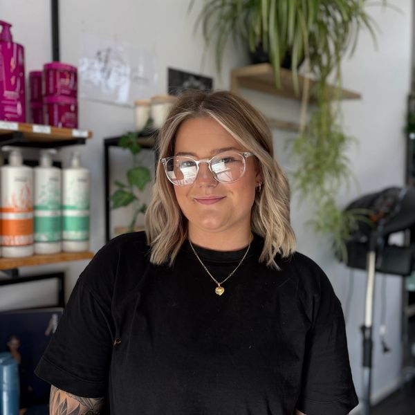 Smiling woman with blonde hair and glasses in a salon setting.