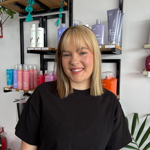 Smiling woman with blonde hair and bangs in a salon setting.