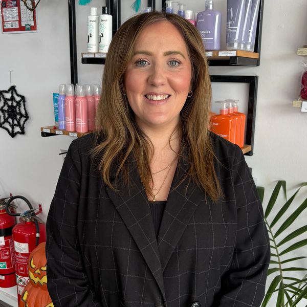 Smiling woman in a black checkered blazer stands in a beauty product store.