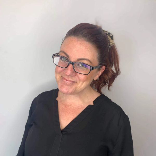 Smiling woman with glasses and a ponytail wearing a black top.