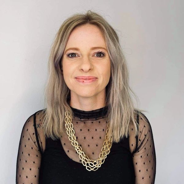 Woman with blonde hair wearing a sheer black top and gold chain necklace.