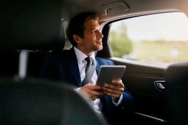 Man in suit using tablet while sitting in car backseat.