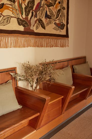 Wooden seating with green cushions and a decorative wall hanging above.