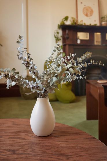 White vase with dried eucalyptus on a wooden table in a cozy living room.