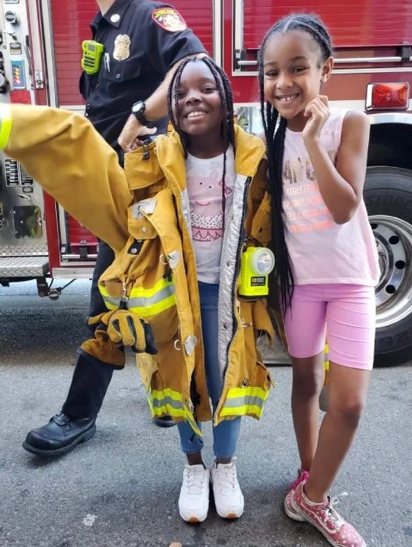 Youth wearing firefighter uniform in front of firetruck.
