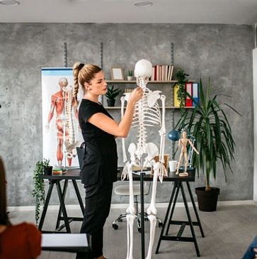 Woman demonstrating human skeleton anatomy in a classroom setting.
